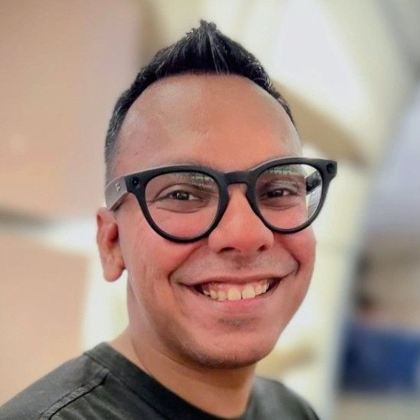 Aditya Pandya, smiling, in round black glasses